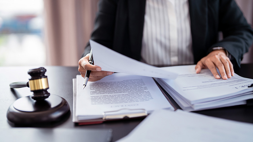Lawyer Reviewing Legal Documents A person in a suit sitting at a desk, reviewing legal documents with a gavel and stacks of papers in front.